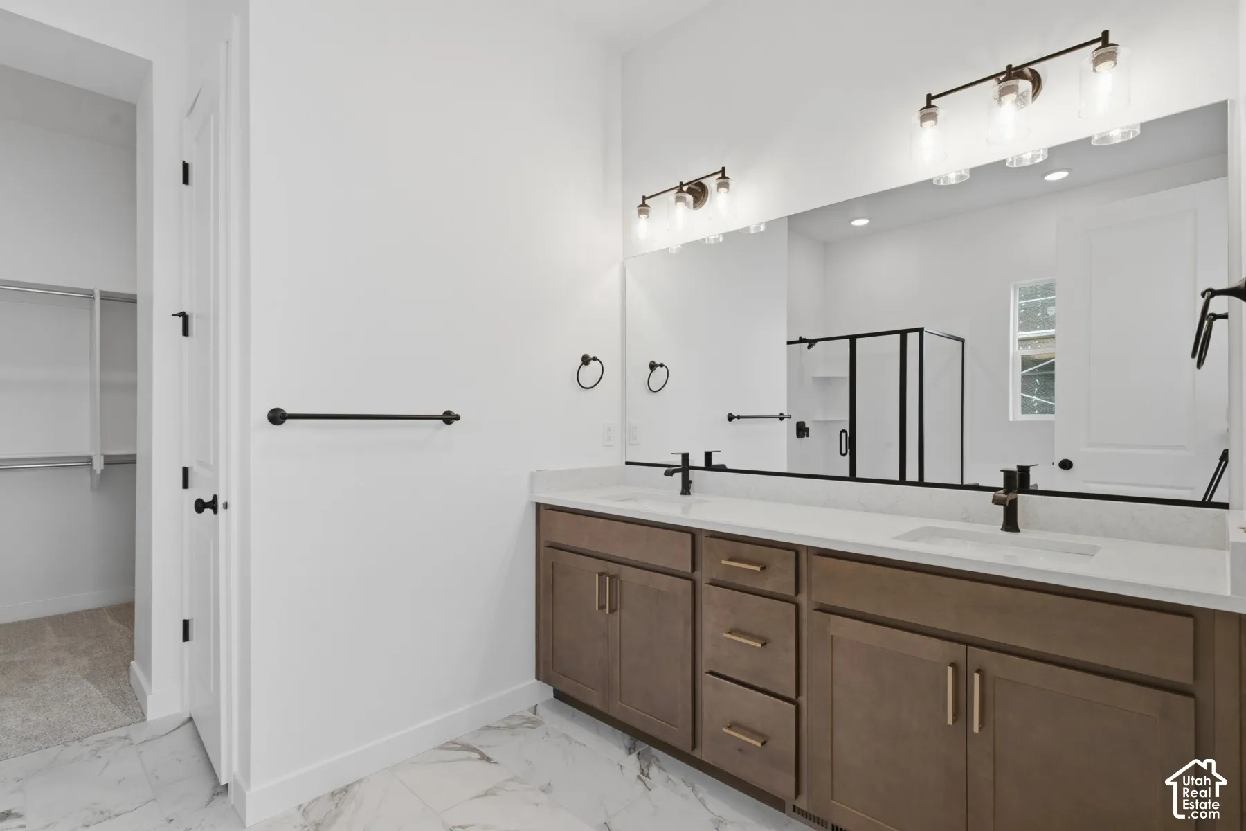 Dual-sink vanity with a solid-surface countertop, integrated rectangular basins, matte black hardware, and wood-finish cabinetry, complemented by full-width vanity mirrors and marble-patterned flooring