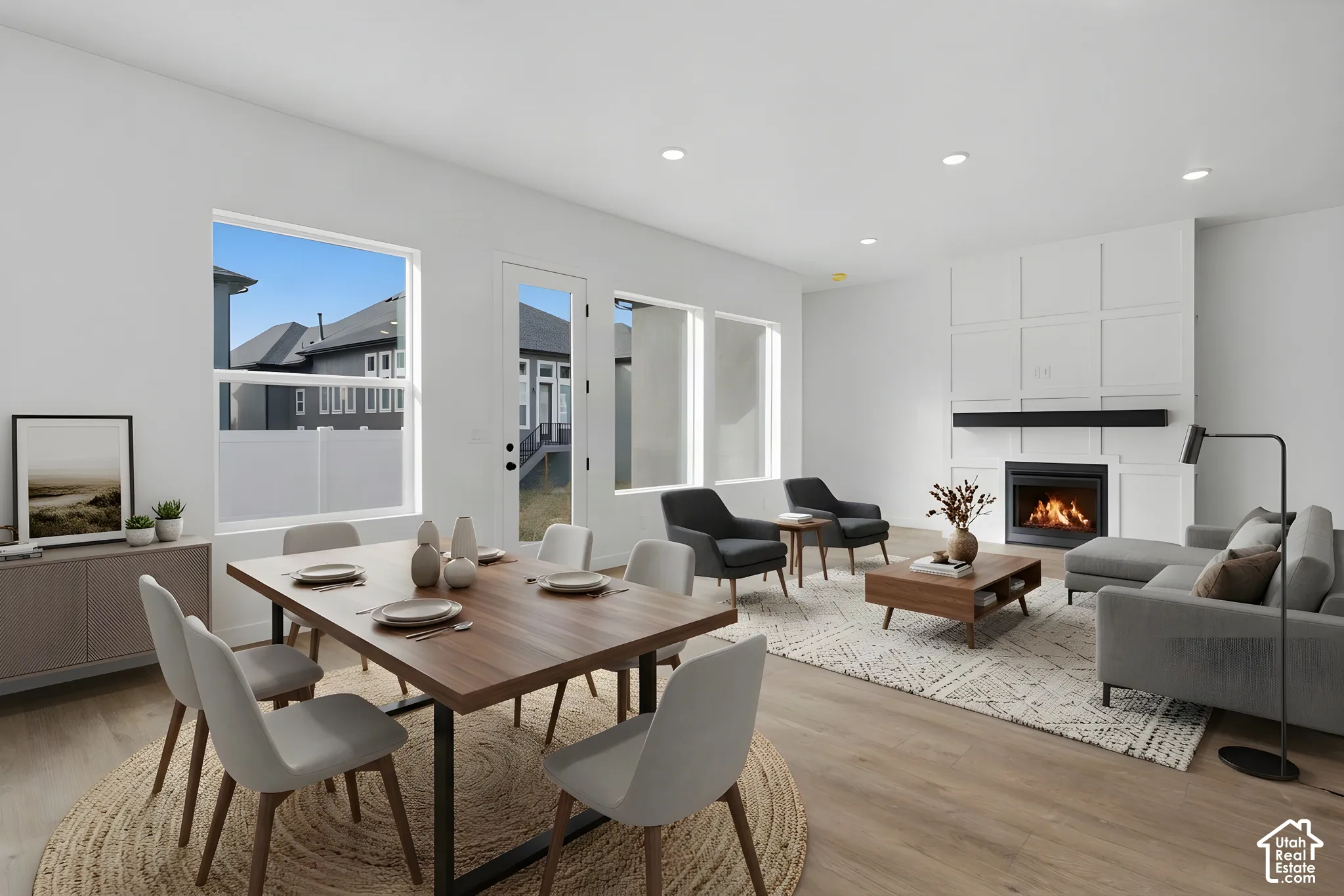 Open-concept area featuring wood-finish flooring, recessed lighting, grid-pattern wall molding, a fireplace with a black mantel, and large windows