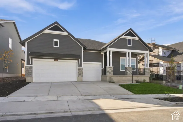 Exterior featuring horizontal lap siding, stone veneer accents, a covered front porch with white columns, and a three-car garage