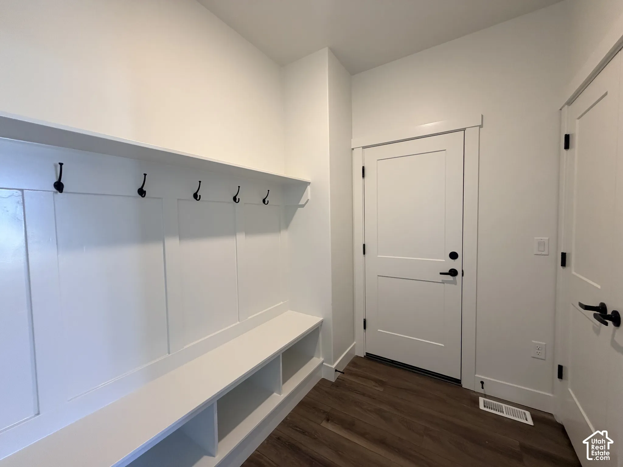 Built-in mudroom bench with integrated storage cubbies, white board-and-batten wall detailing, overhead shelving with wall-mounted hooks, solid-core shaker style doors, and wood-finish flooring