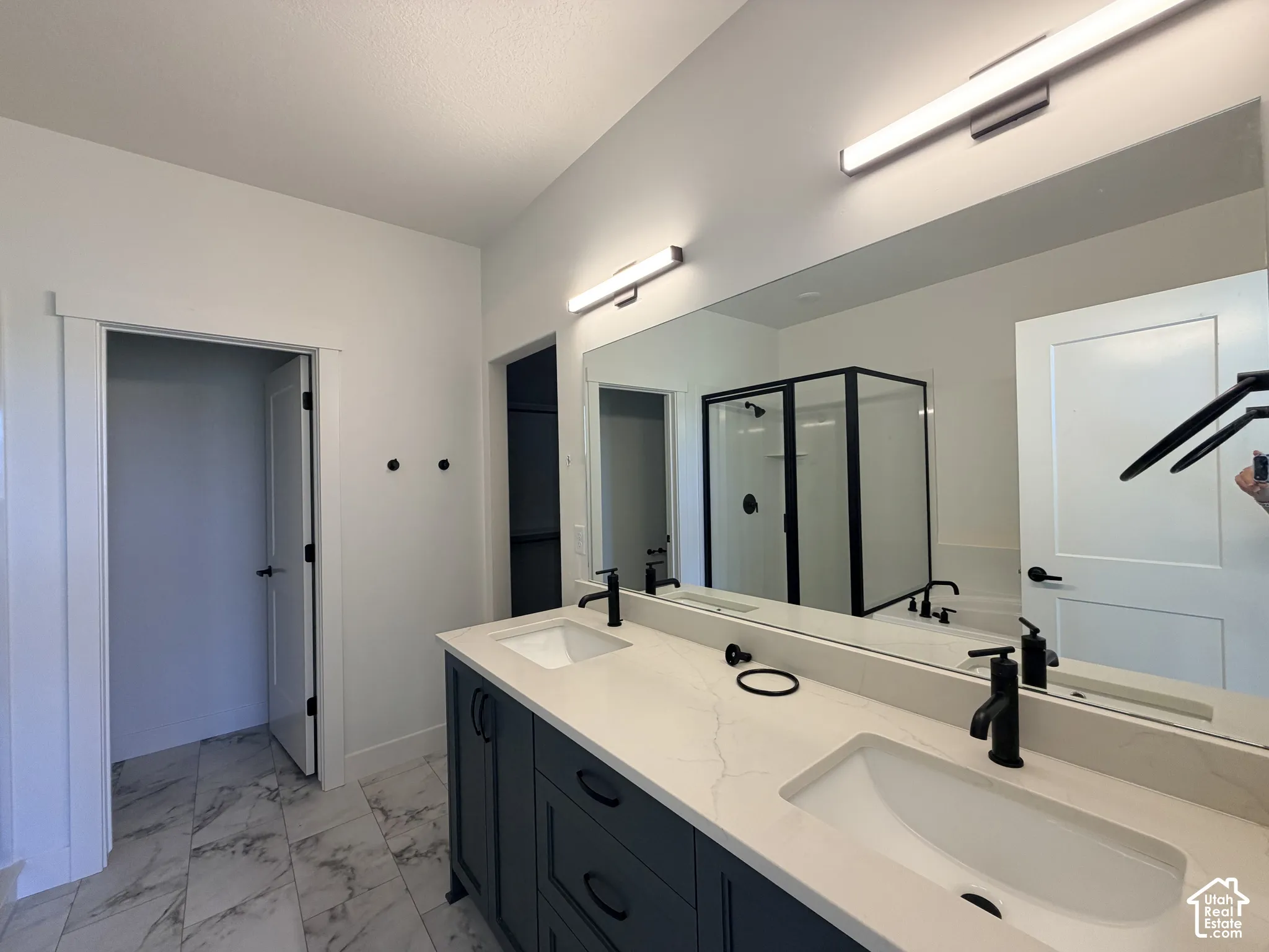 Dual-sink vanity with matte black fixtures, quartz countertops, full-width mirror, contemporary linear wall lighting, and tiled flooring