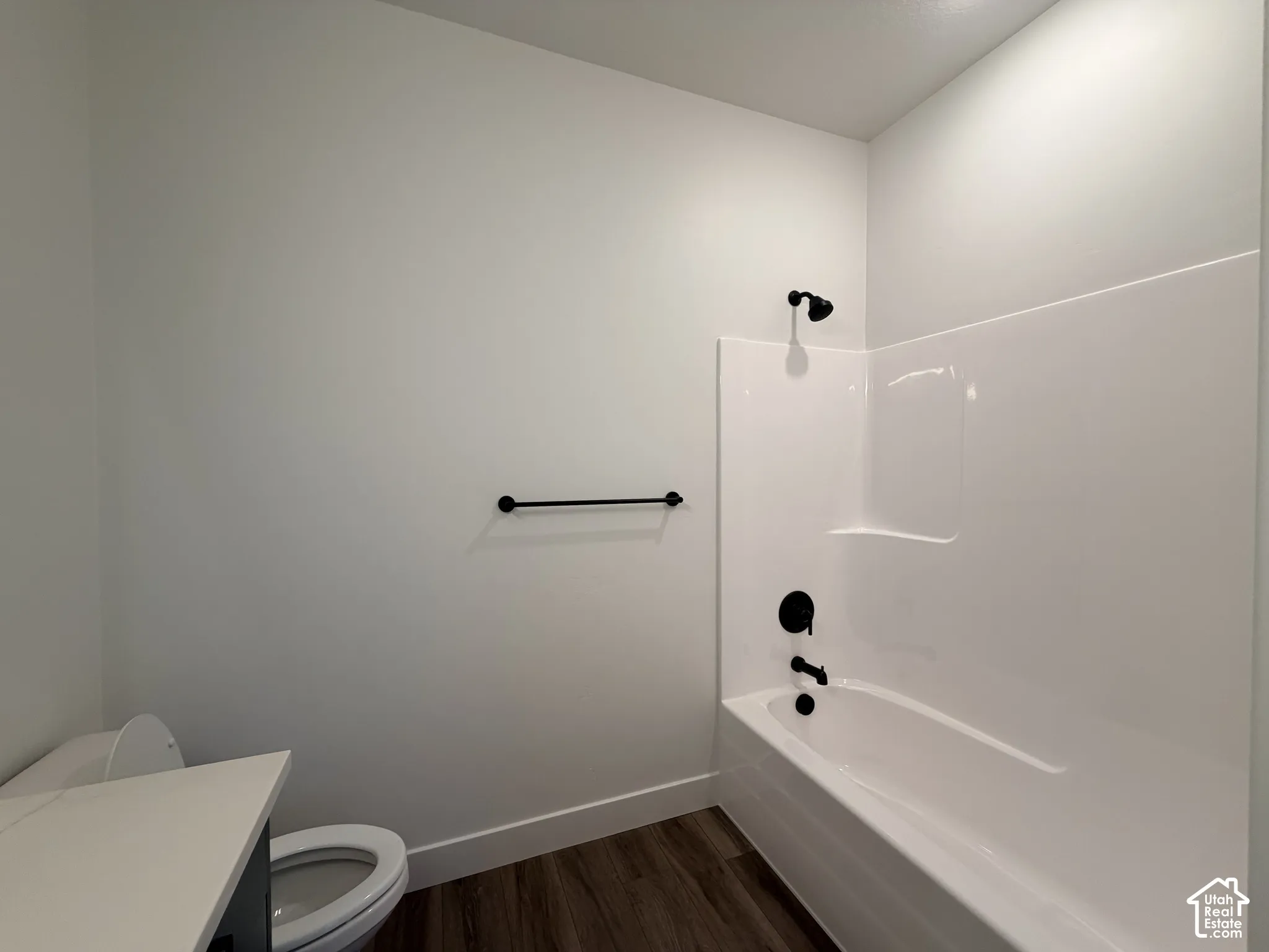 Full bathroom featuring wood-finish flooring, a white acrylic tub surround, and matte black plumbing fixtures, including a wall-mounted towel bar