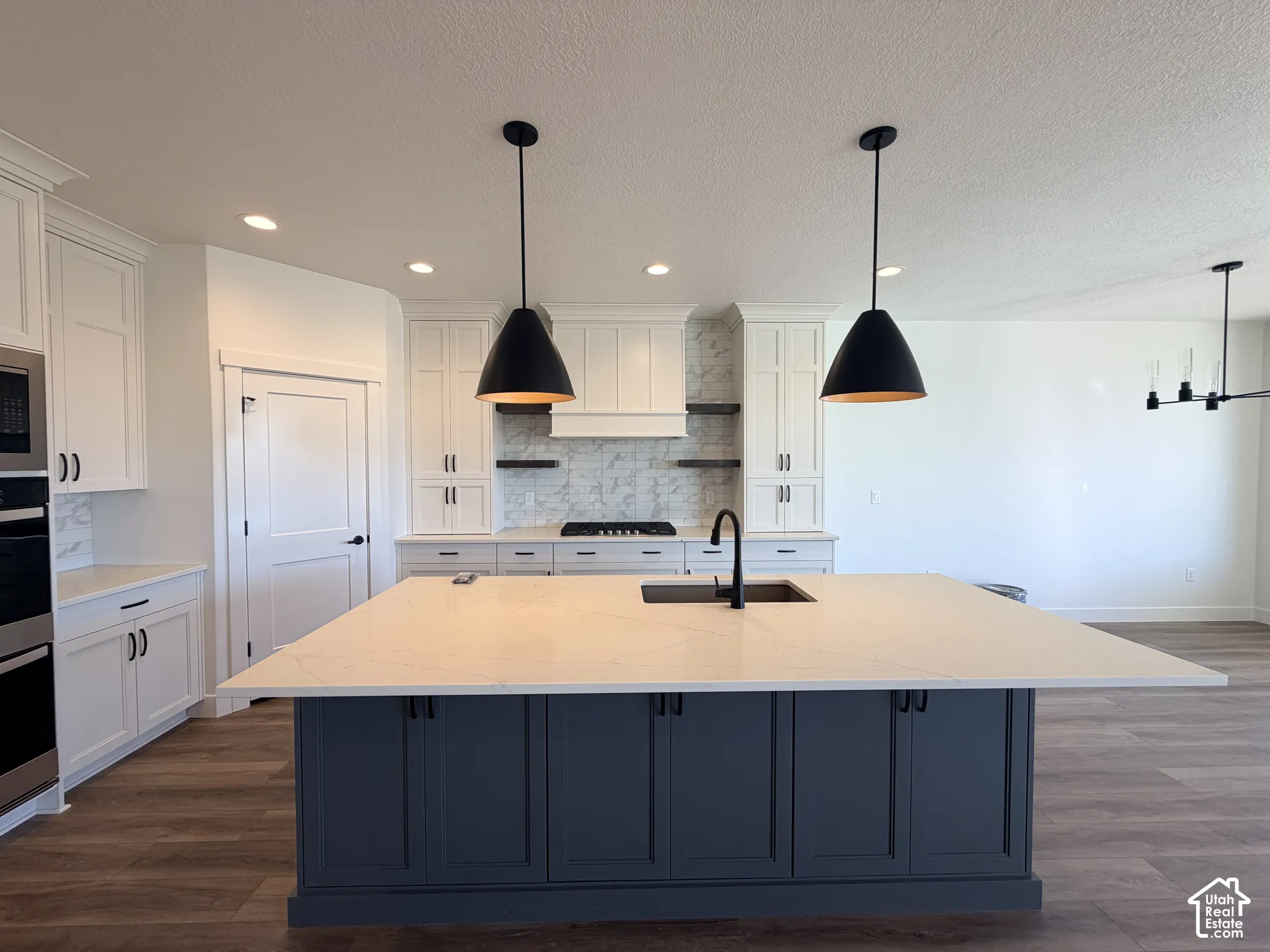 Kitchen featuring a large central island with solid-surface countertop, custom cabinetry, matte black pendant lighting, gas cooktop with range hood, and wood-finish flooring