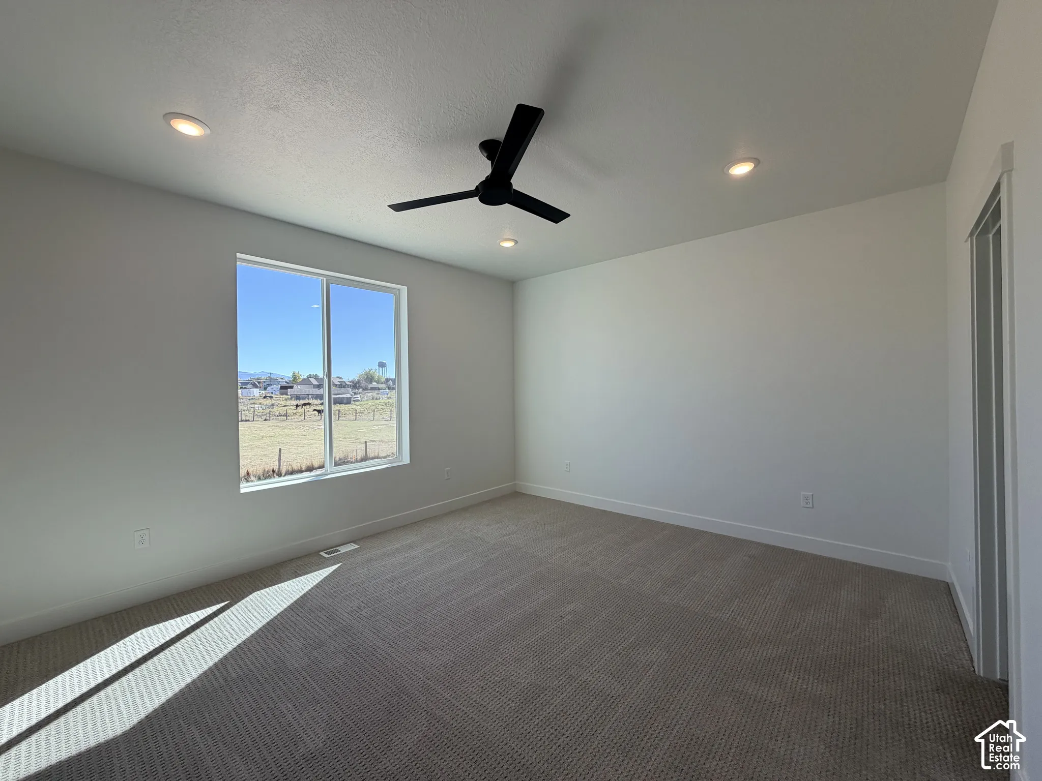 Neutral-toned wall-to-wall carpeting, matte black three-blade ceiling fan, recessed lighting, and a single-pane window