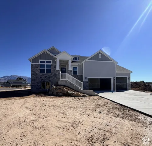 Exterior featuring a mix of stone veneer and horizontal siding, mountain backdrop, covered entryway with white railing, and a three-car garage