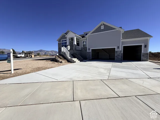 Exterior featuring a light-toned siding facade, stone veneer accents, multi-car garage, concrete driveway, and covered porch entrance