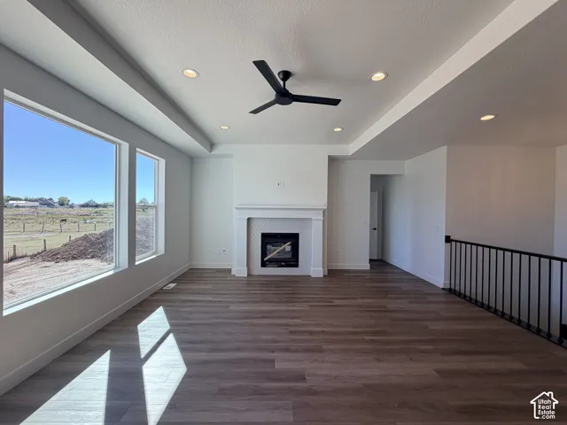Living area featuring wood-finish flooring, recessed lighting, a tray ceiling, a fireplace with a decorative mantel, and metal stair railing