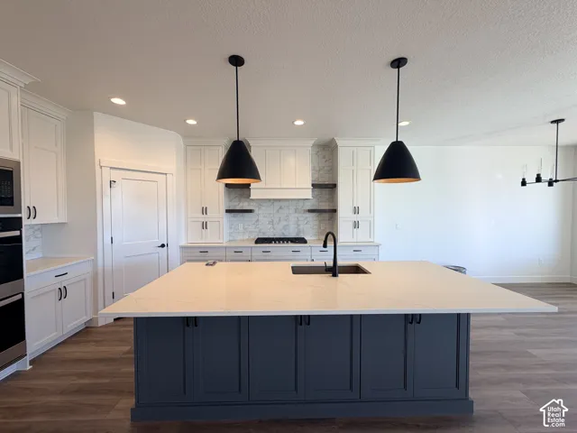 Kitchen featuring a large central island with solid-surface countertop, custom cabinetry, matte black pendant lighting, gas cooktop with range hood, and wood-finish flooring