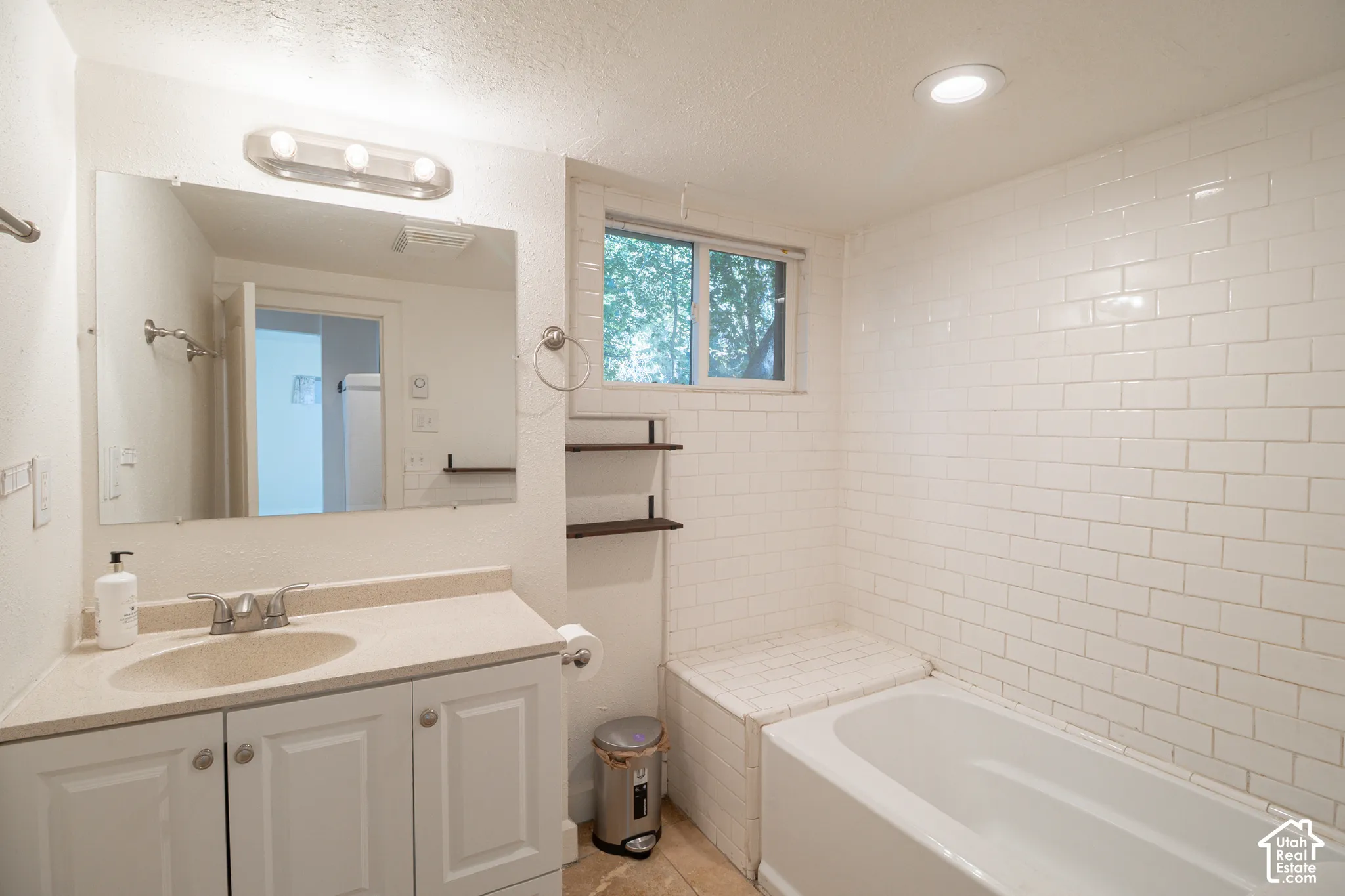 Bathroom featuring white subway tile surround, built-in tub bench, recessed lighting, wall-mounted vanity with solid surface countertop, and integrated sink