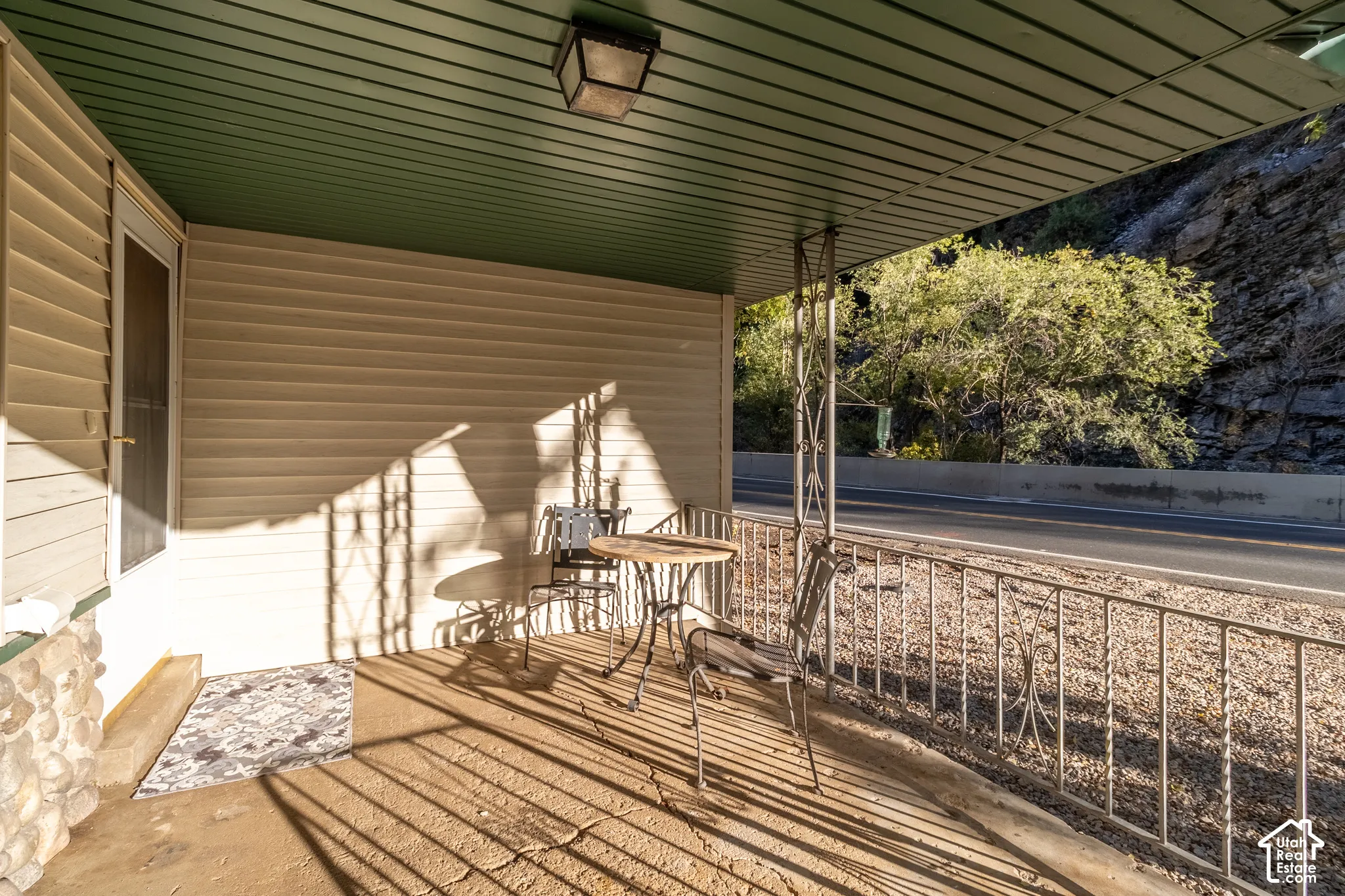 Covered porch featuring light-toned horizontal siding, a stone veneer base, metal decorative railings, and a solid-surface concrete floor