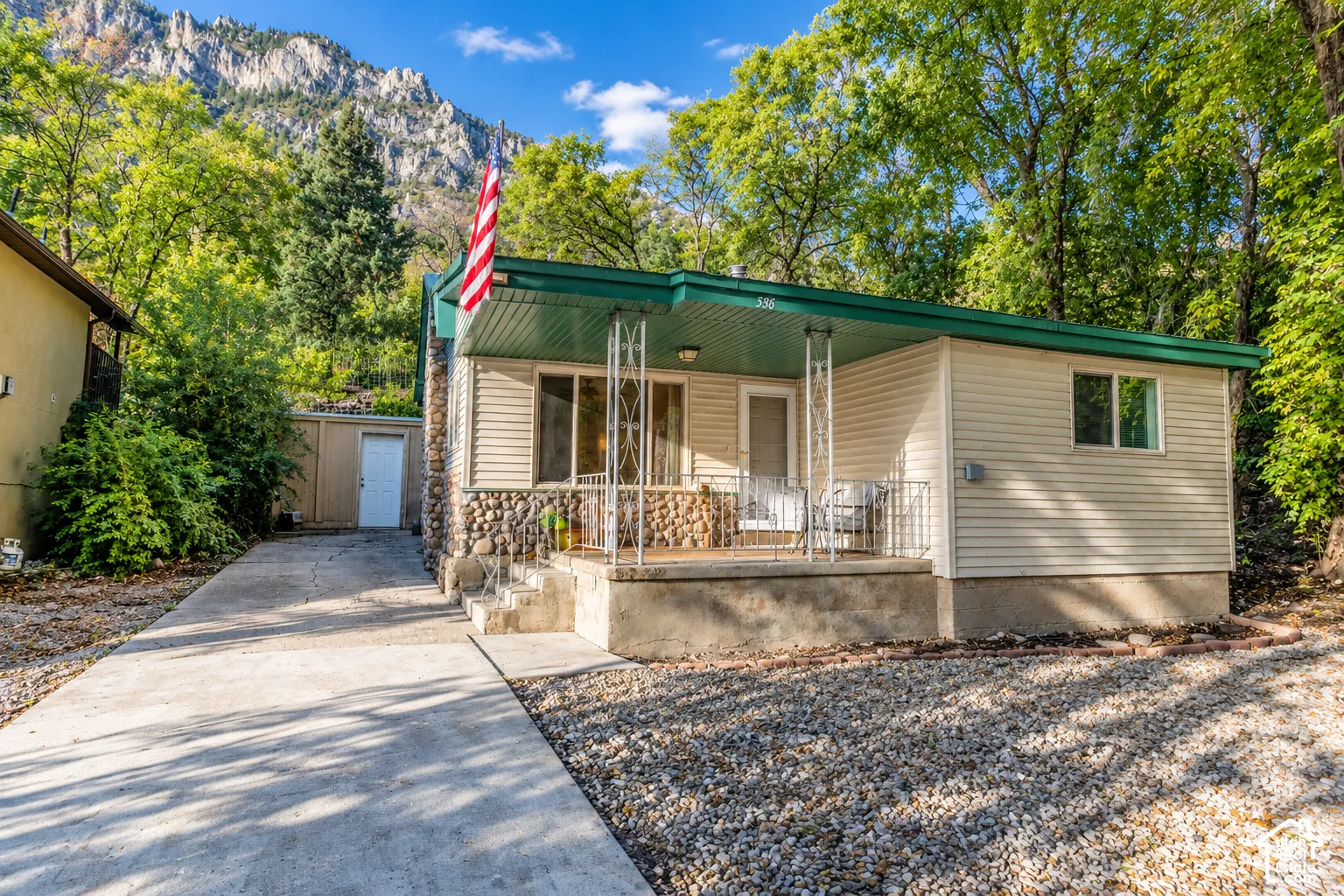 Exterior featuring horizontal siding, a river stone facade, a covered front porch with decorative iron columns, and a concrete driveway leading to a detached garage
