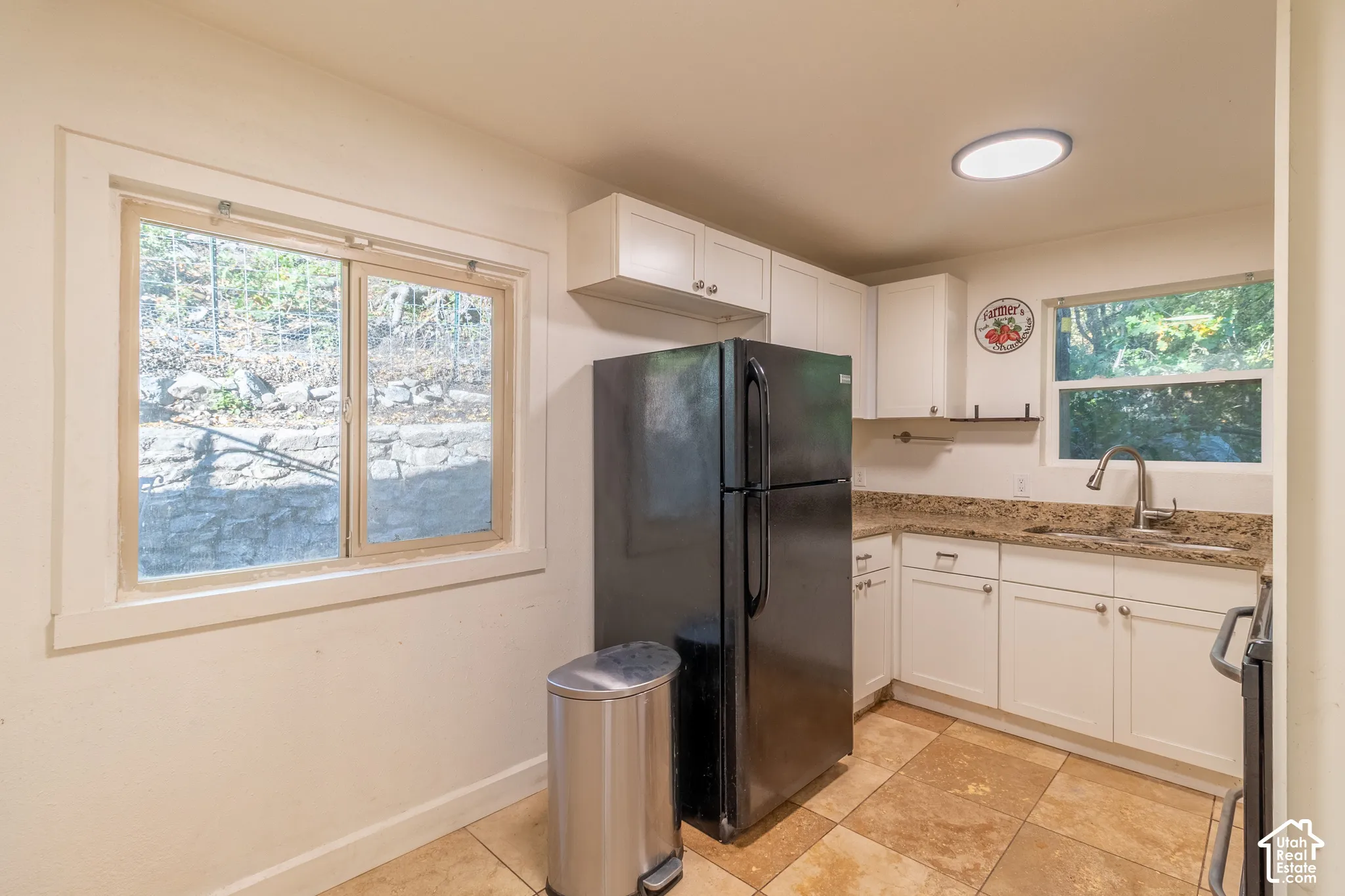 Kitchen featuring white shaker-style cabinetry, natural stone countertops, tile flooring, and dual windows