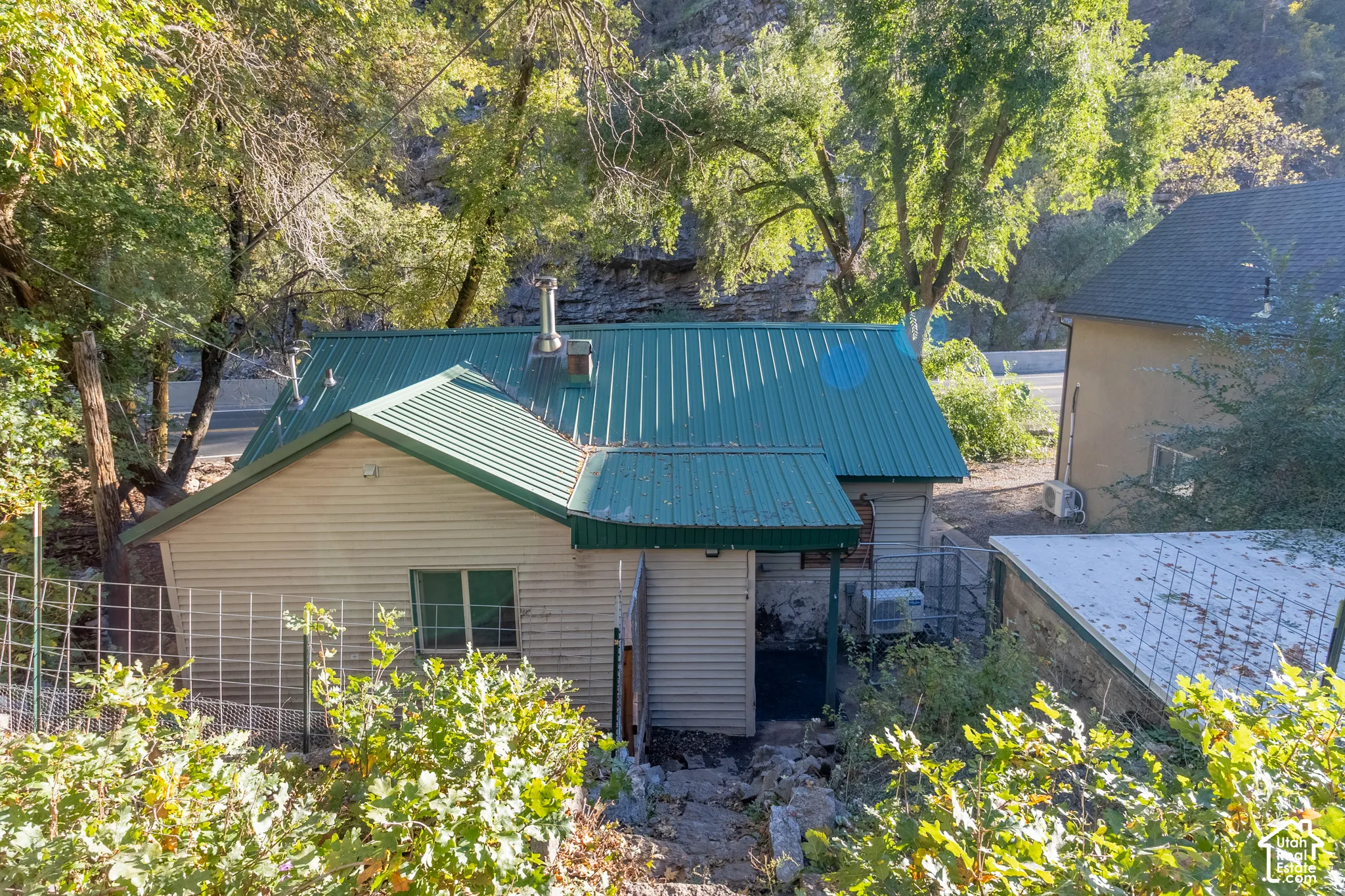 Exterior featuring a green metal roof, siding, and stone foundation elements, set within a wooded landscape with natural rock formations