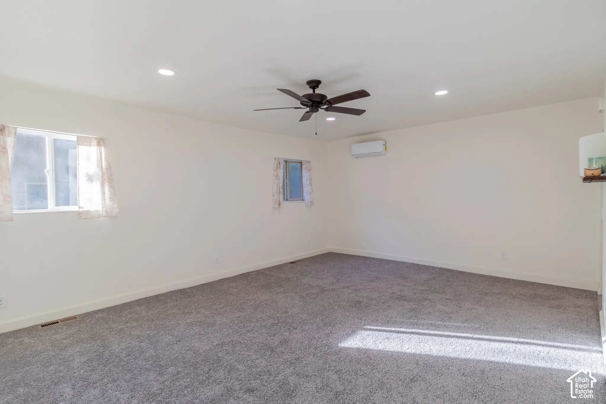 Neutral-toned carpeted flooring, recessed lighting, wall-mounted ductless mini-split system, and a ceiling fan