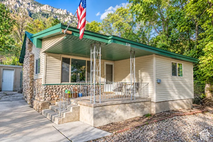 Exterior featuring lap siding, stone veneer facade, covered front porch with metal railing, and concrete steps, set against a backdrop of mountain terrain