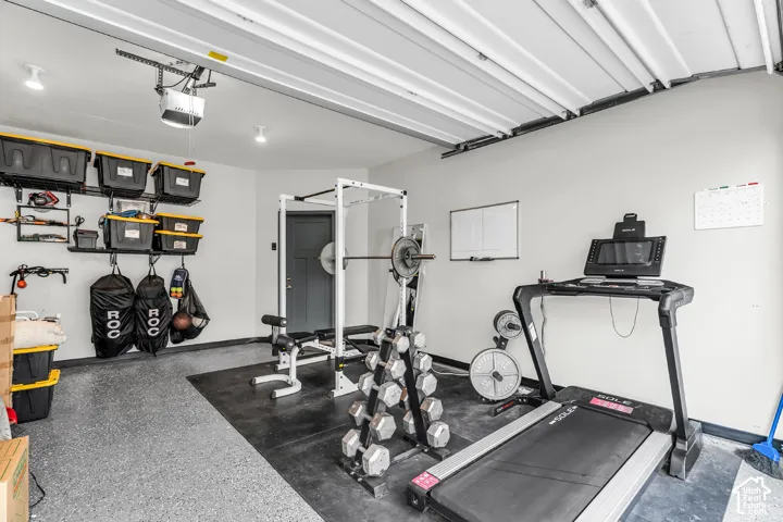 Garage space featuring finished walls, an epoxy-coated concrete floor, an automated overhead door opener, and a wall-mounted shelving system