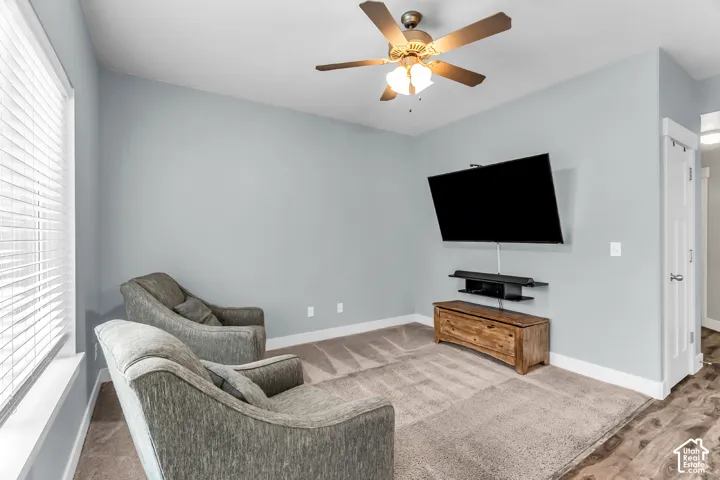 Room featuring neutral wall tones, wood-finish flooring, carpeting, a ceiling fan with integrated lighting, and a multi-pane window with blinds