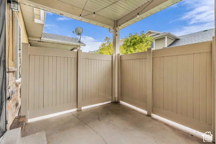 Covered concrete patio featuring stone veneer siding, privacy fencing, and exterior light fixtures