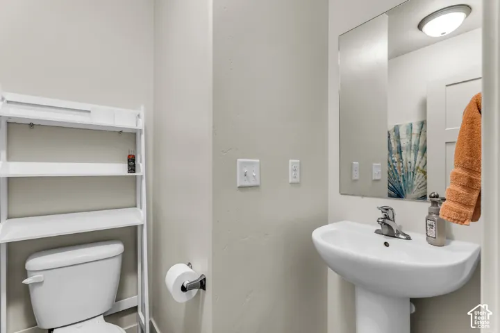 Wall-mounted mirror, pedestal sink with a single-handle faucet, and ceramic toilet