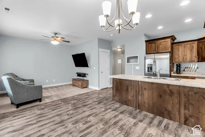 Open-concept area featuring wood-finish flooring, a kitchen island with stone-finish countertops, natural wood cabinetry, a multi-arm chandelier, and recessed lighting