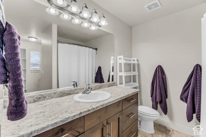 Bathroom featuring a wood-finish vanity with a stone-composite countertop, integrated sink basin, multi-bulb vanity lighting, and a large wall-mounted mirror