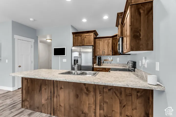 Kitchen featuring a central island with a stone-finish countertop, stainless steel refrigerator, stained wood cabinetry, and wood-finish flooring
