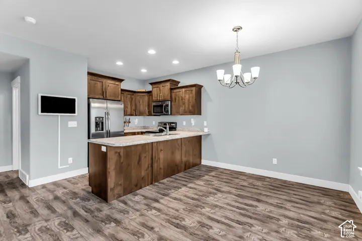 Kitchen featuring stained wood cabinetry, stone-finish countertops, stainless steel appliances, wood-finish flooring, and a multi-light chandelier
