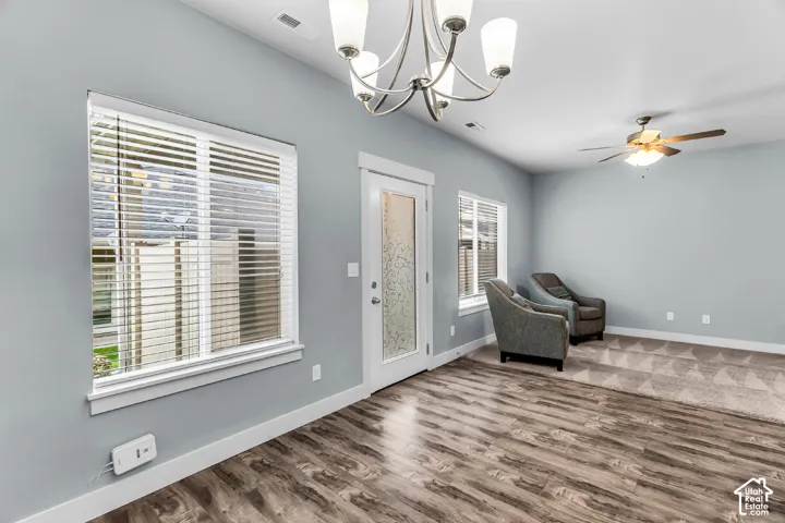 Wood-finish flooring, multi-light chandelier, ceiling fan with integrated lighting, and a glass-paneled exterior door