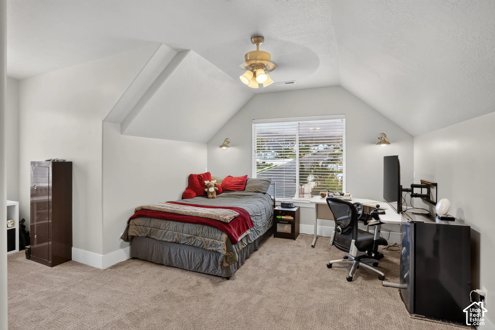 Vaulted ceilings, neutral carpeting, window with integrated blinds, ceiling fan with light kit, and wall-mounted sconce lighting