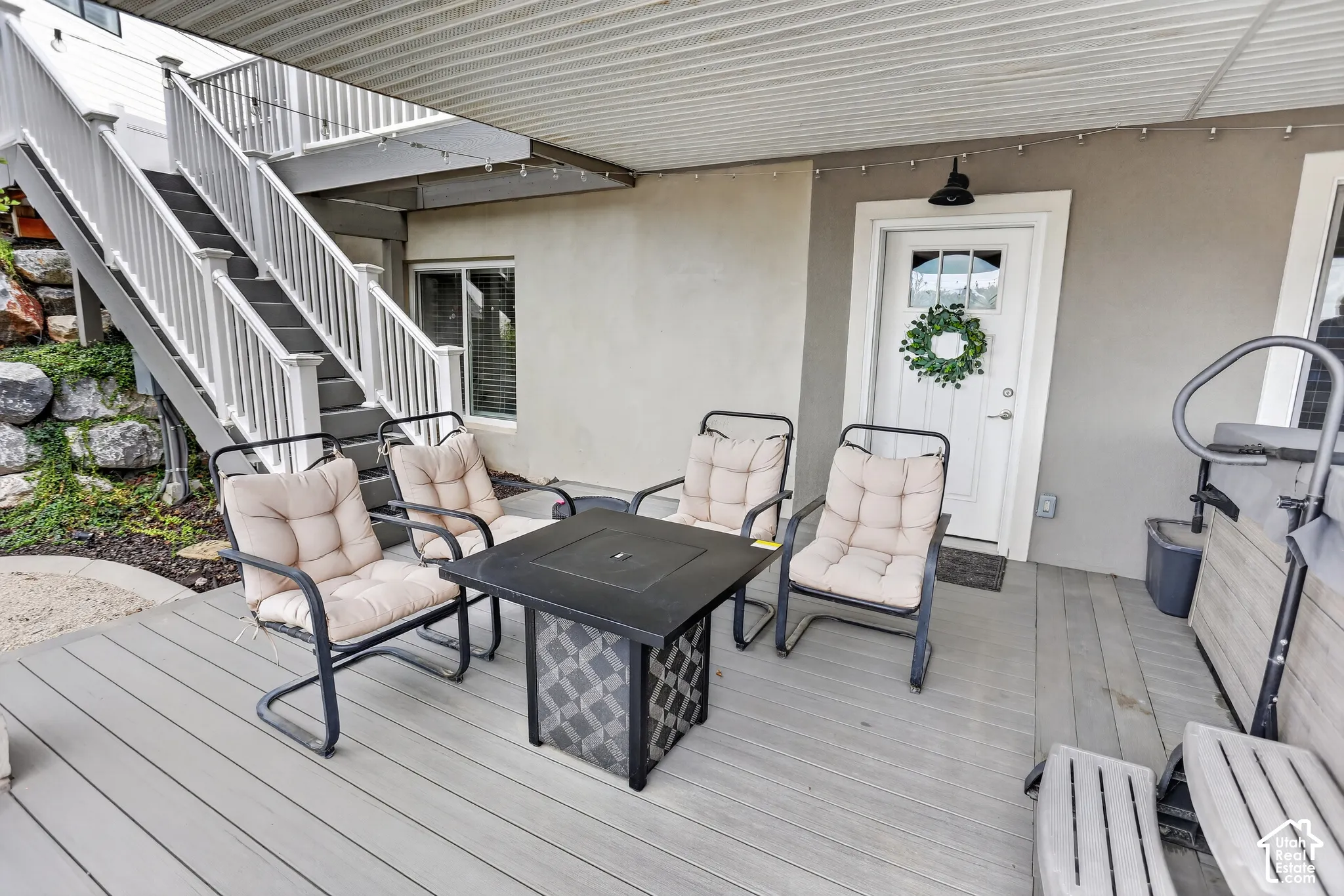 Covered patio featuring composite decking, exterior staircase with white railings, and direct access through a paneled door