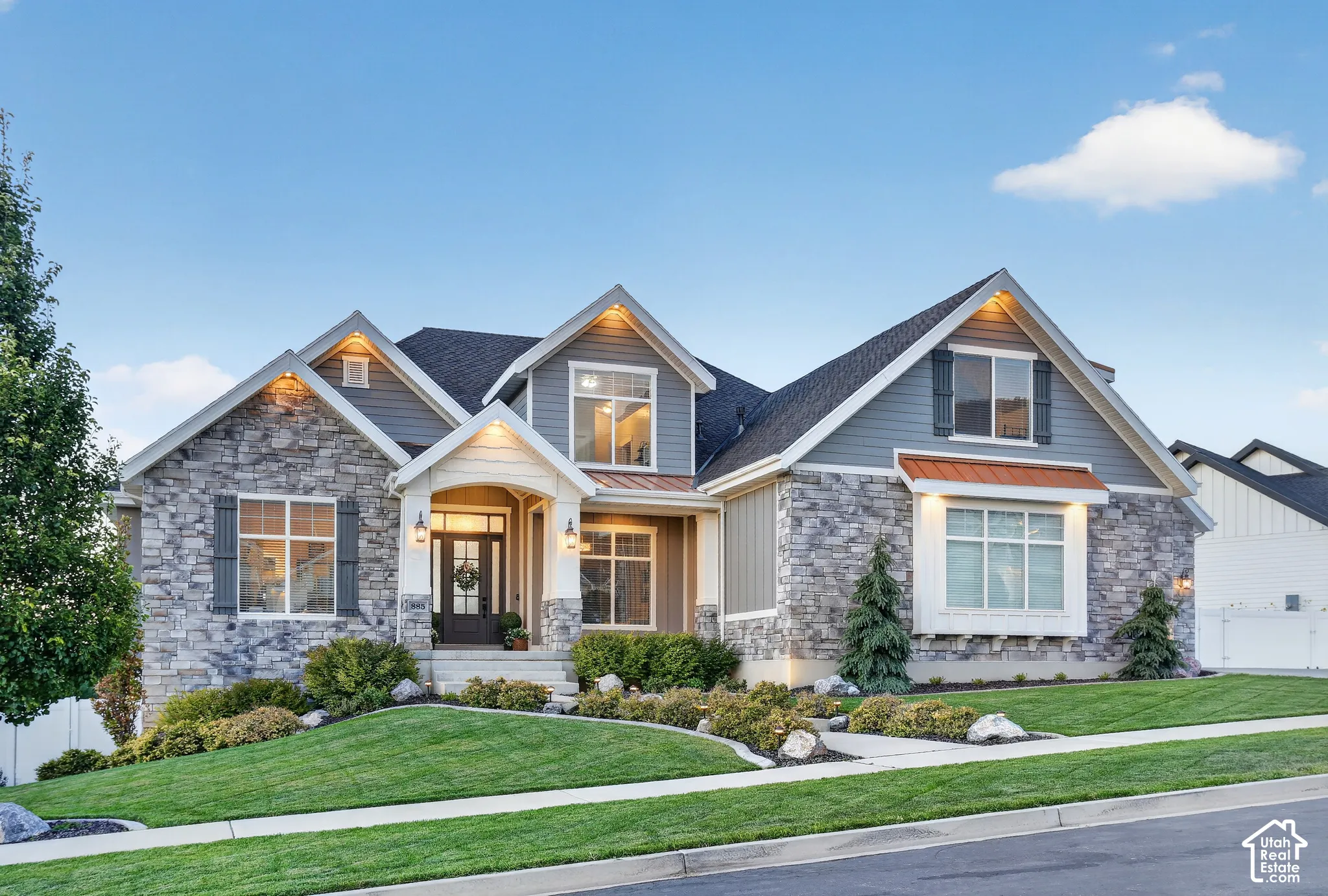 Multi-gabled exterior featuring stone veneer siding, horizontal lap accents, copper-toned metal roofing details, and a covered entry with a glass-paneled front door