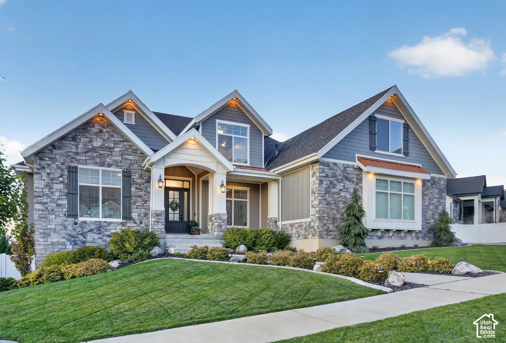 Exterior facade featuring stacked stone masonry, horizontal lap siding, multi-gabled rooflines, copper-finished metal awnings, and a covered entryway