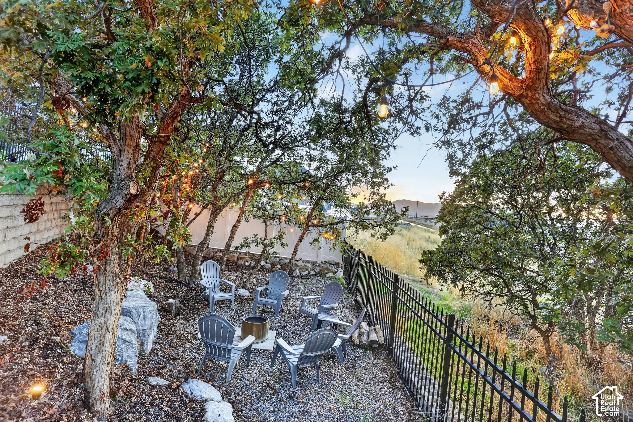 Private outdoor space featuring mature trees, a metal perimeter fence, and large decorative boulders