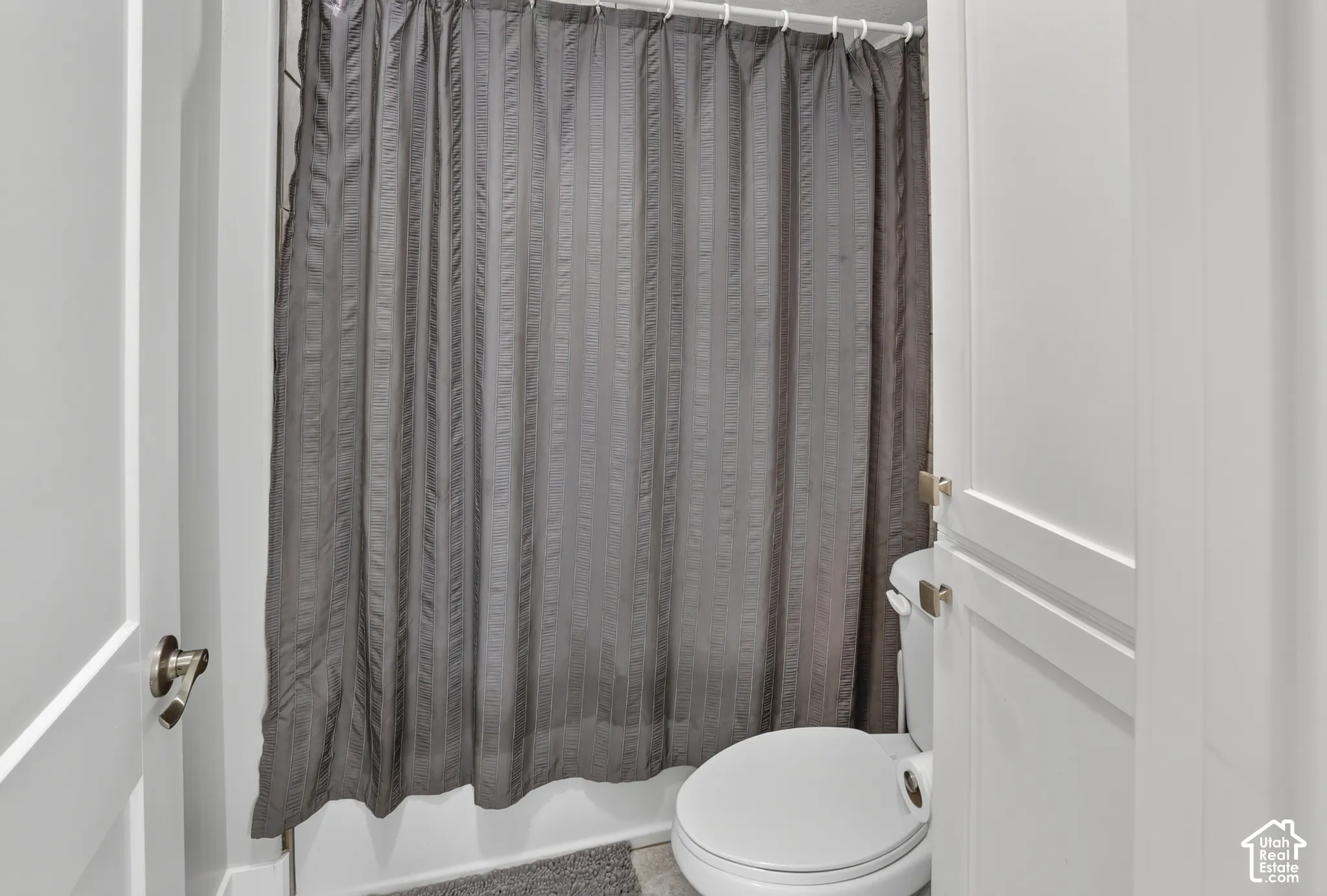 Bathroom featuring a white toilet, floor-to-ceiling cabinetry with white panel doors, and a shower area enclosed by a curtain