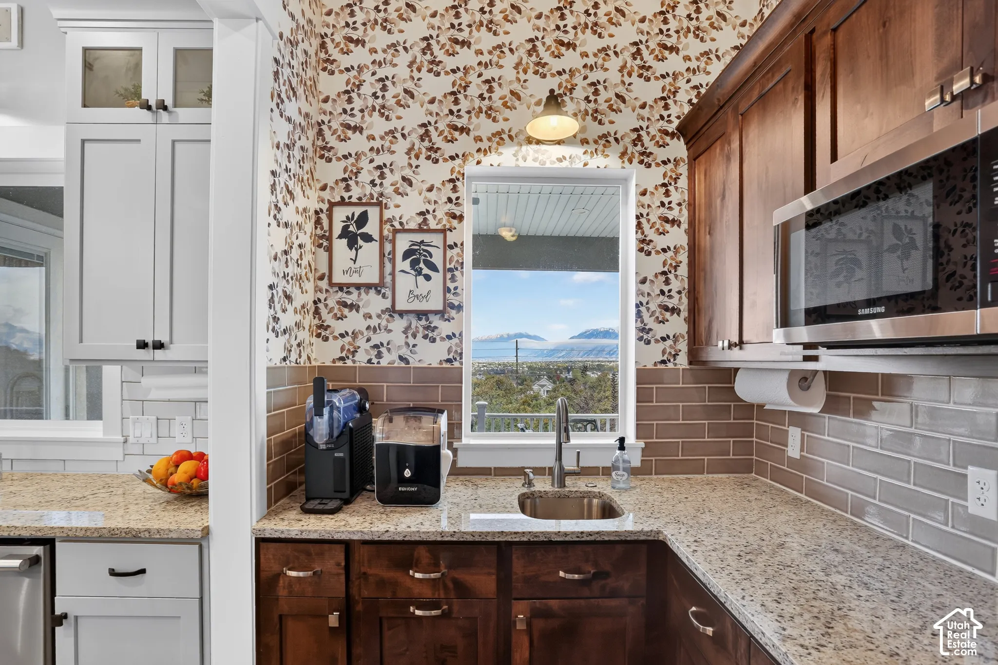 Kitchen area featuring dark wood cabinetry, light-toned stone-surface countertops, horizontal tile backsplash, integrated stainless steel microwave, and exterior mountain scenery visible through the window