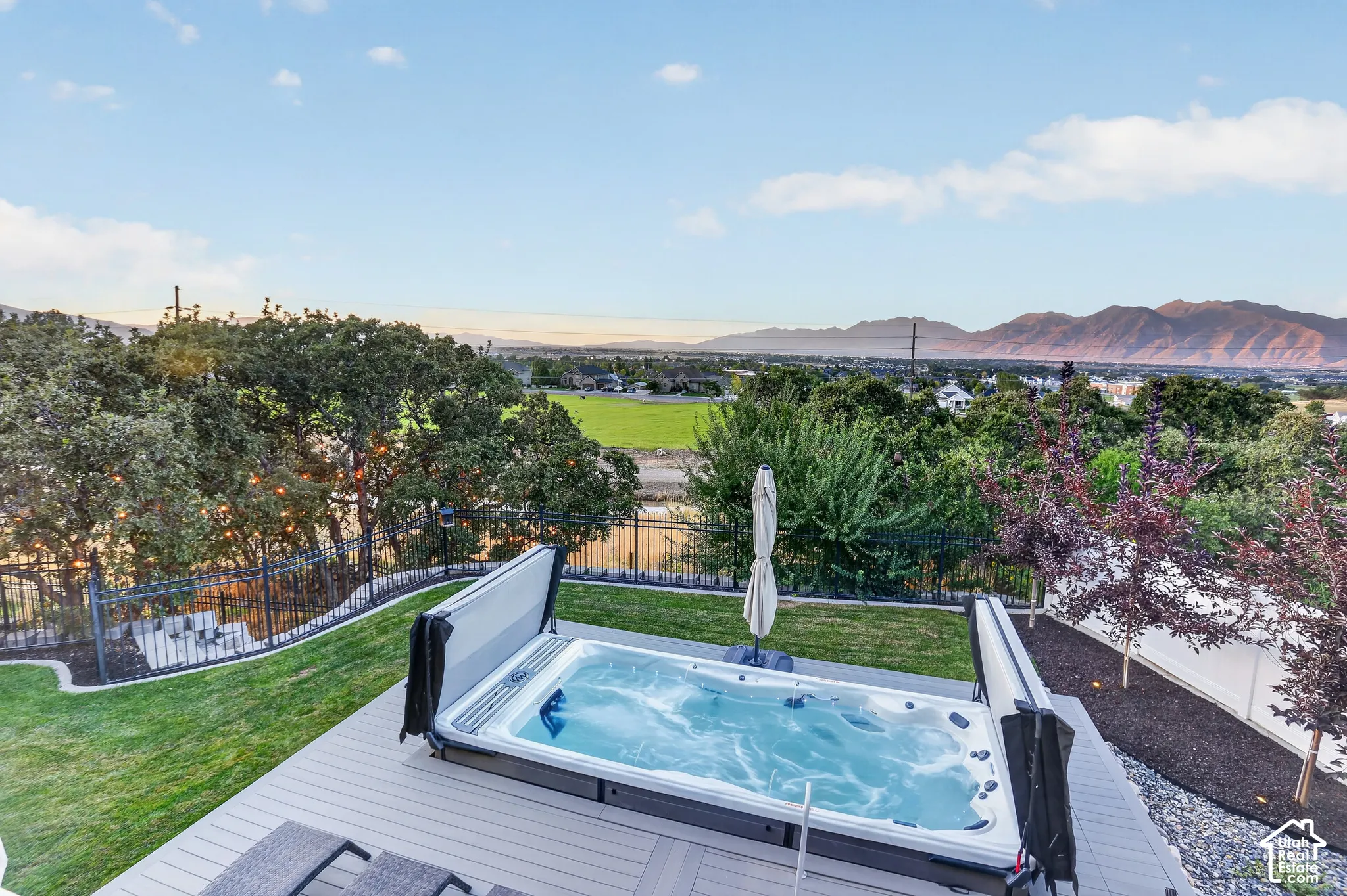 Backyard featuring a built-in jetted swim spa, composite decking, manicured lawn, perimeter metal fencing, and a mountainous backdrop