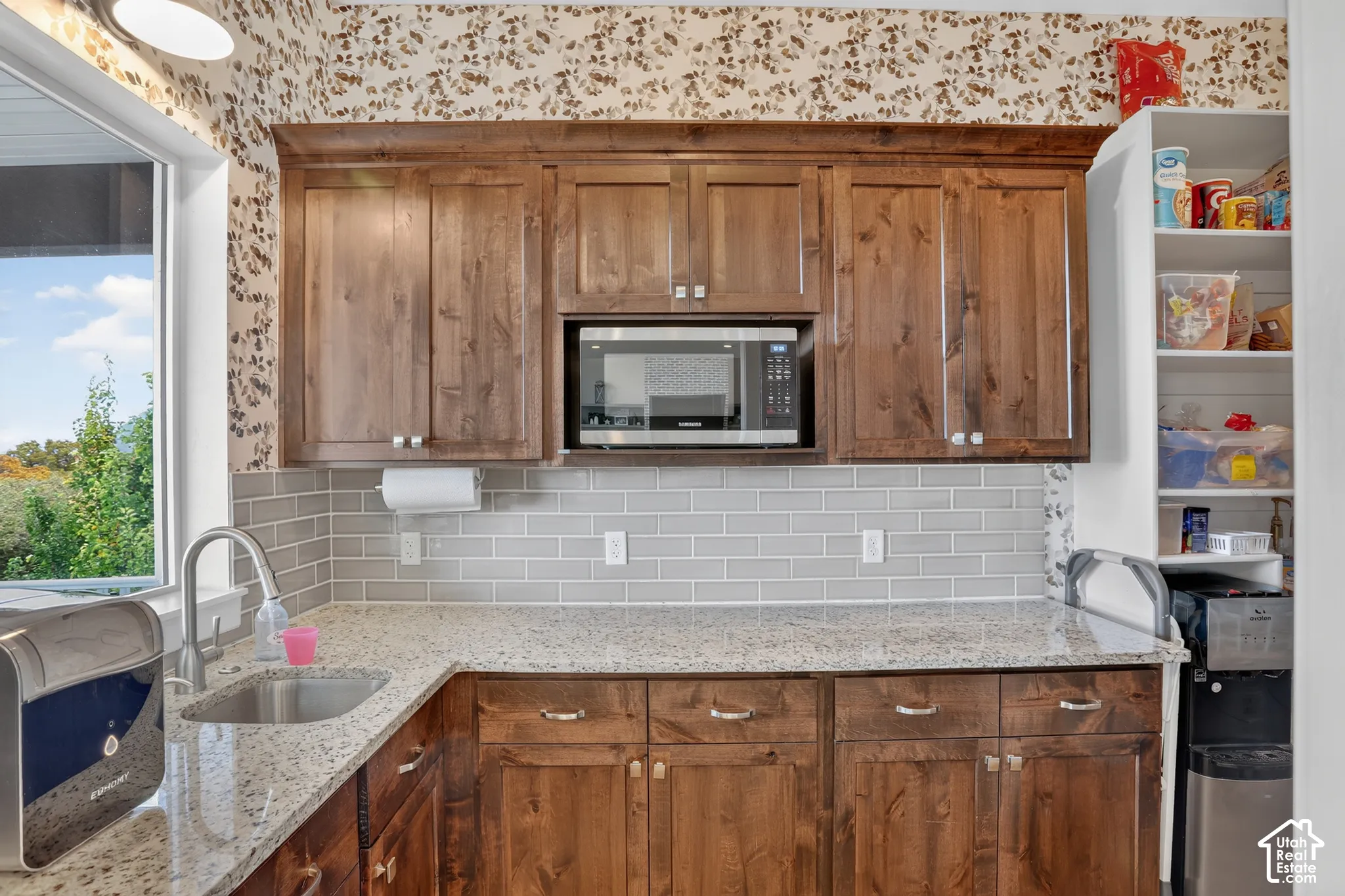 Stained wood cabinetry with built-in microwave, stone-surface countertops, subway tile backsplash, stainless steel undermount sink, and integrated shelving