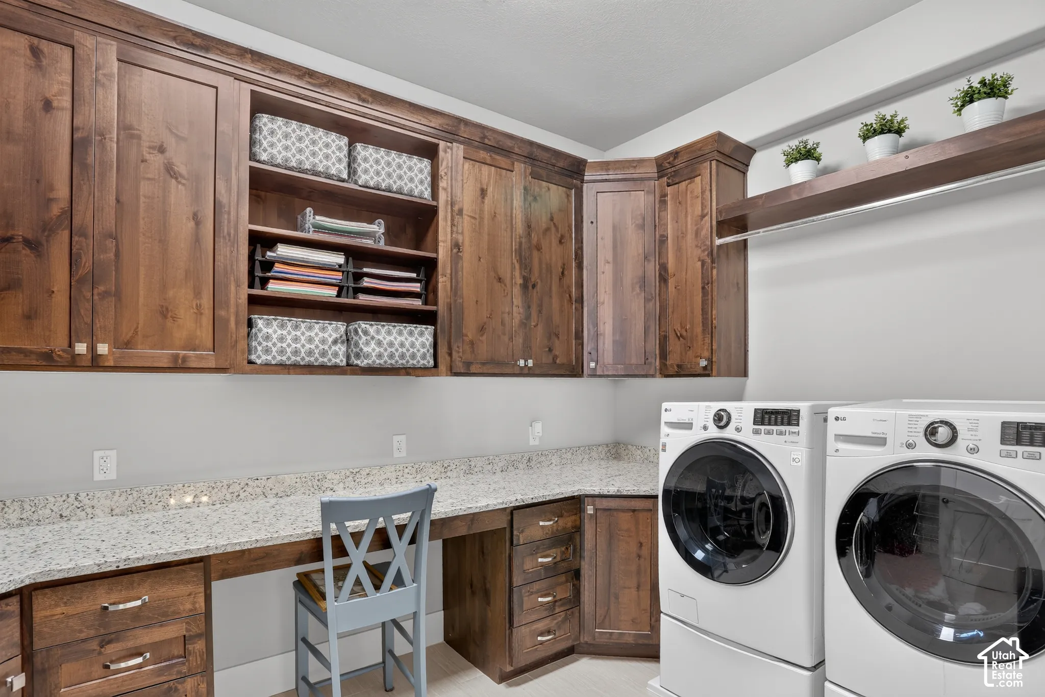 Custom stained wood cabinetry, stone-surface countertop, built-in desk area, integrated drawers, and open wall-mounted shelving