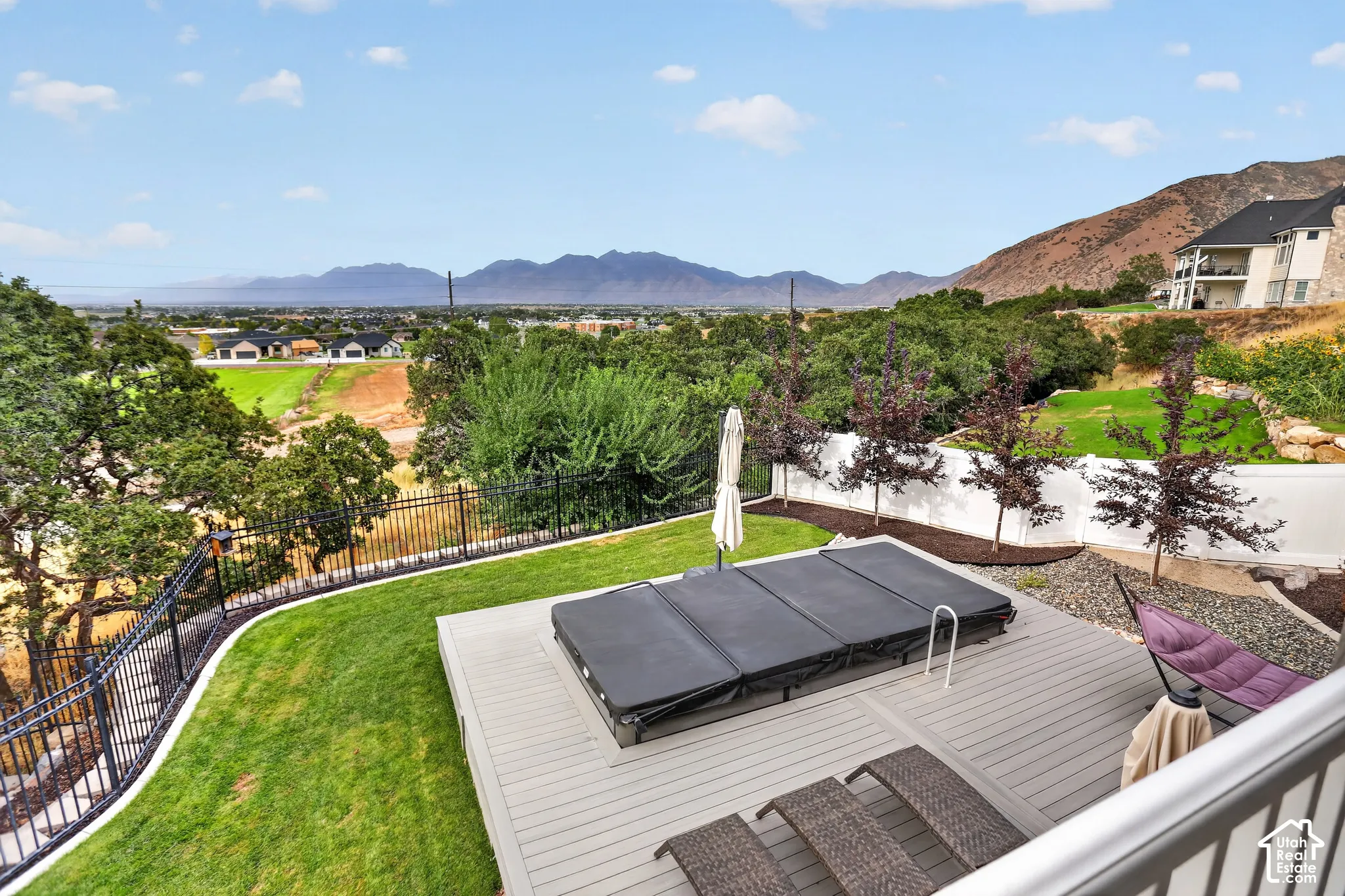 Backyard featuring a composite deck with an inset hot tub, manicured lawn, tiered landscaping, and mountain backdrop