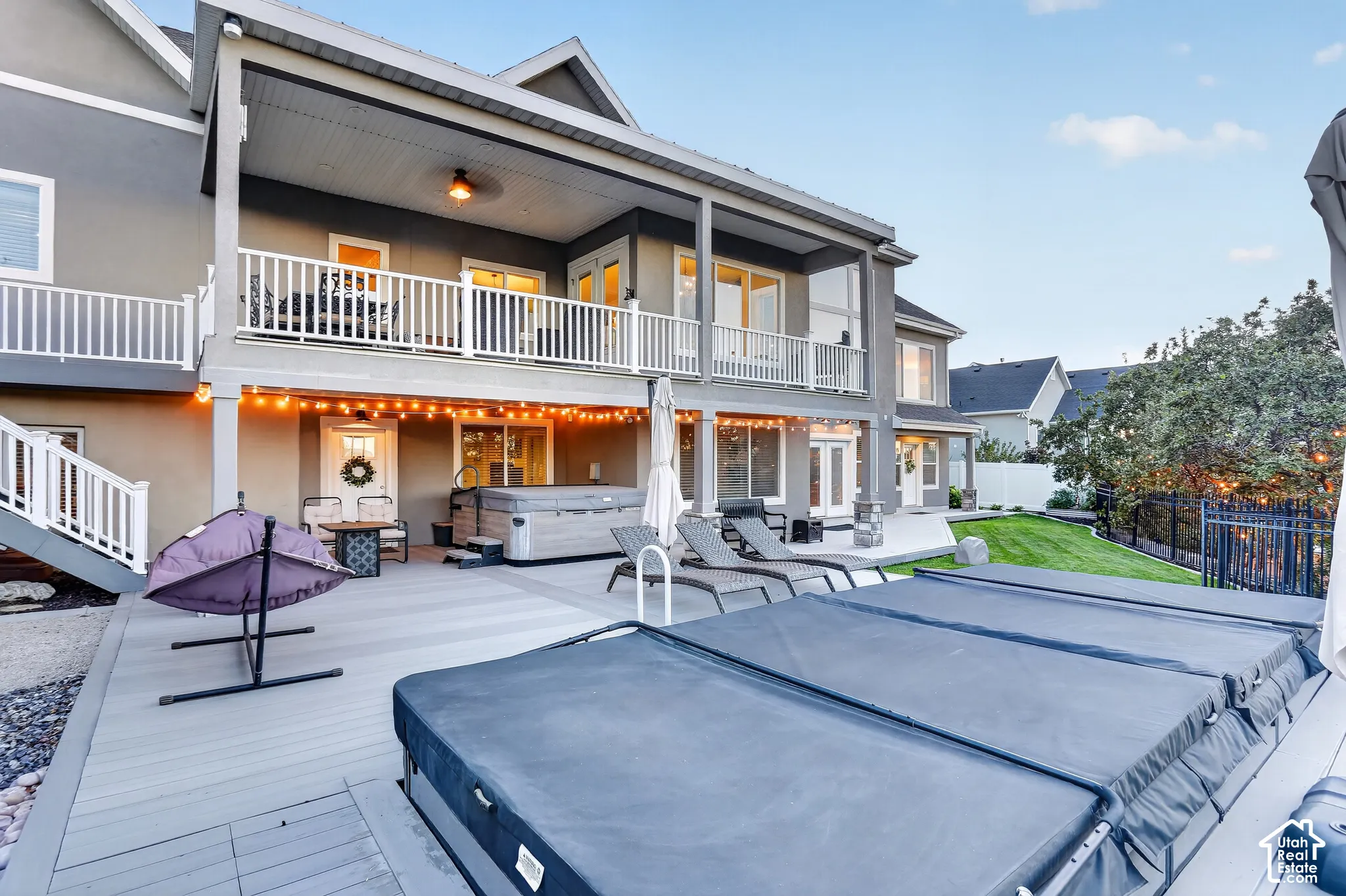 Multi-level exterior featuring a covered upper-level deck with white railings, a expansive lower-level composite deck, an in-ground pool, a hot tub, and a manicured lawn
