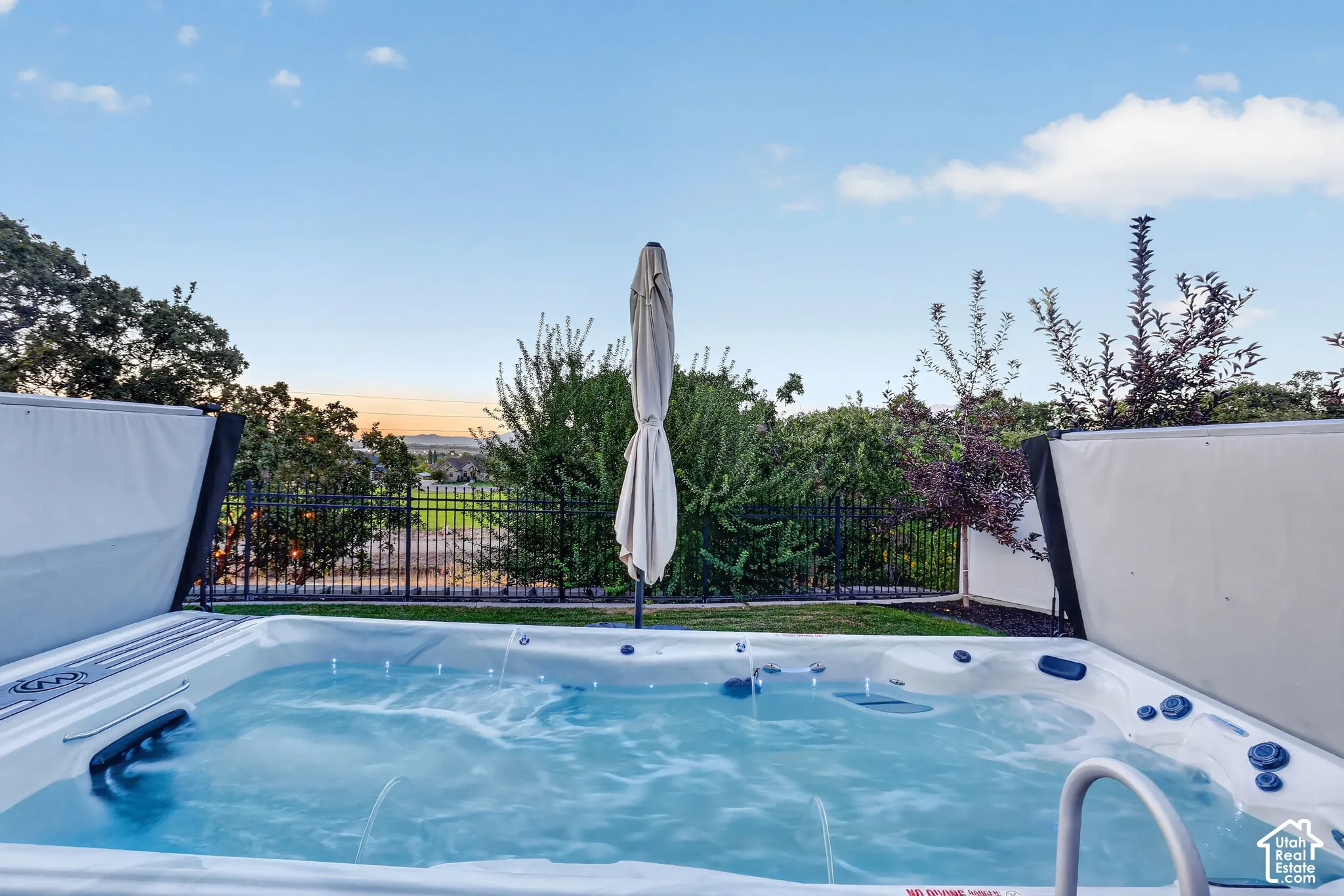 Custom in-ground spa featuring integrated water jets, an expansive lawn, and black metal perimeter fencing
