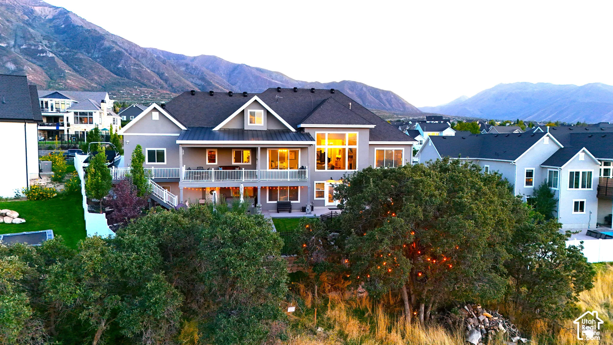 Multi-level residence featuring a gray siding exterior, expansive upper-level deck with white railing, and floor-to-ceiling windows, set against a prominent mountain backdrop