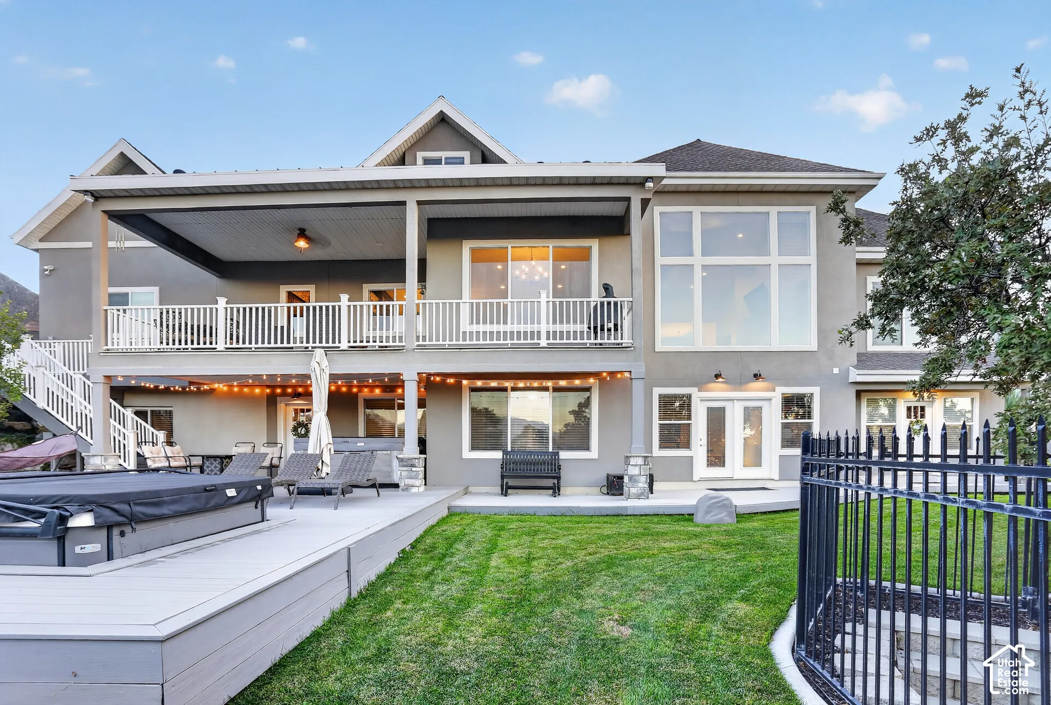 Two-story exterior featuring a covered upper-level deck, expansive floor-to-ceiling windows, a ground-level patio, and fenced yard