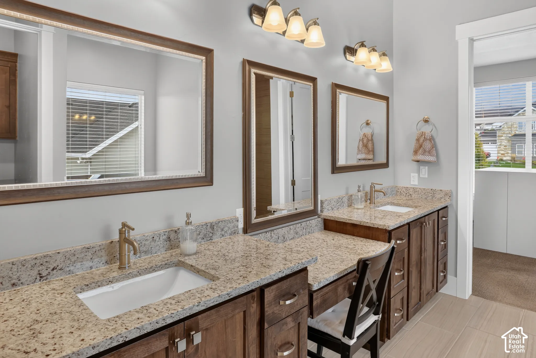 Double vanity with stone-surface countertops, undermount sinks, wood-finish cabinetry, and framed wall mirrors