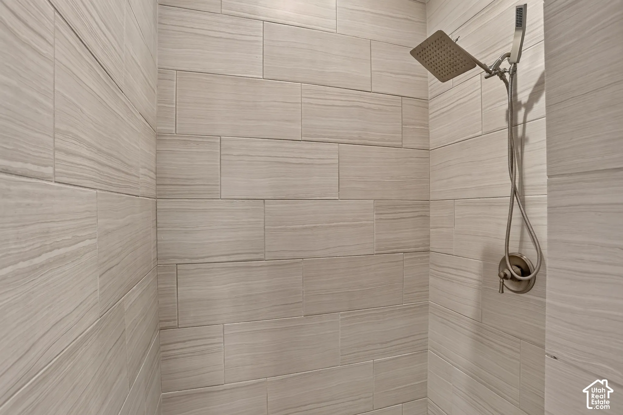 Shower enclosure featuring neutral-toned linear tile surround, a brushed metal rainfall shower head, a handheld sprayer attachment, and a single-handle temperature control valve