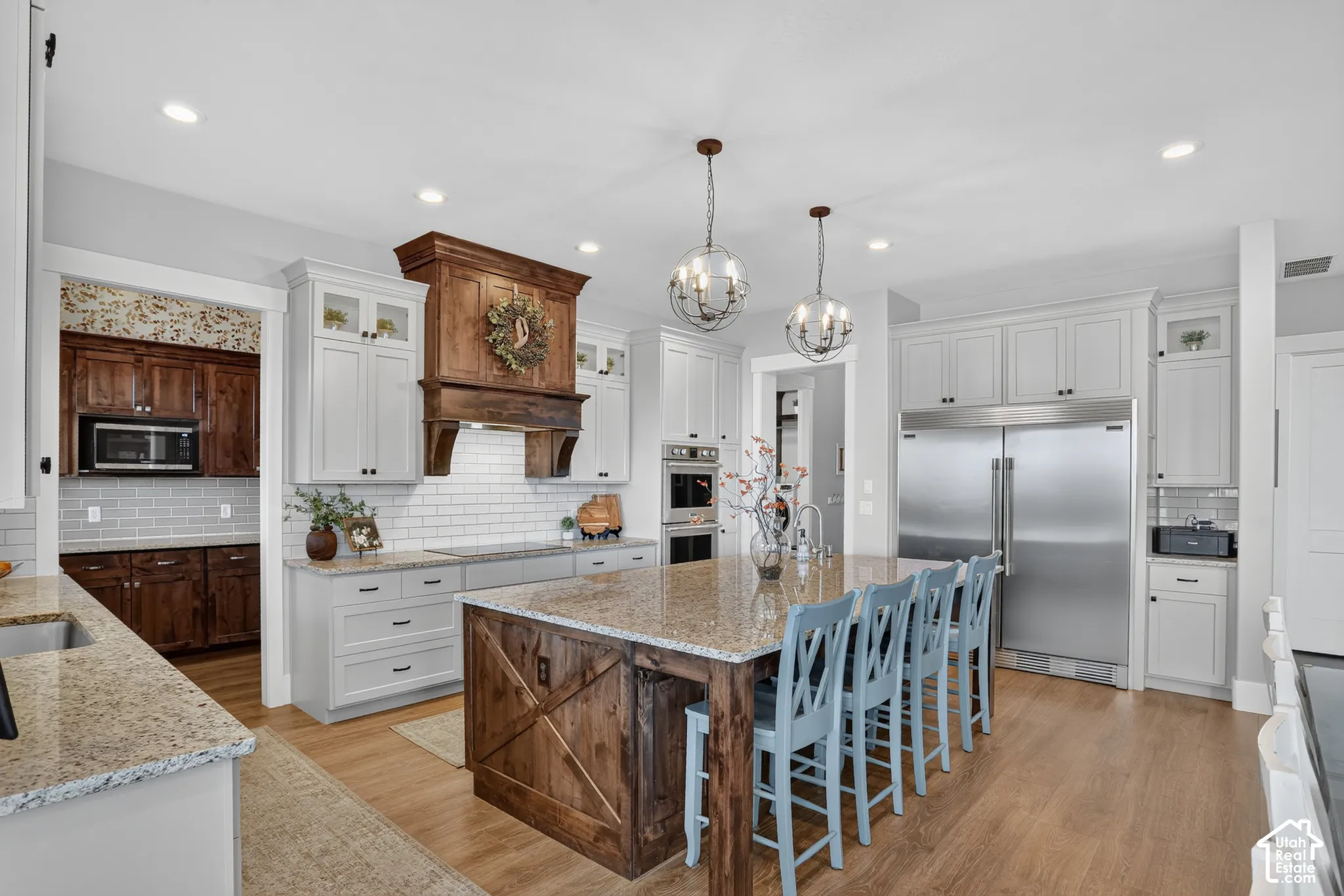 Kitchen featuring custom cabinetry, a central island with natural stone countertops, a wood-trimmed range hood, stainless steel appliances, and recessed lighting