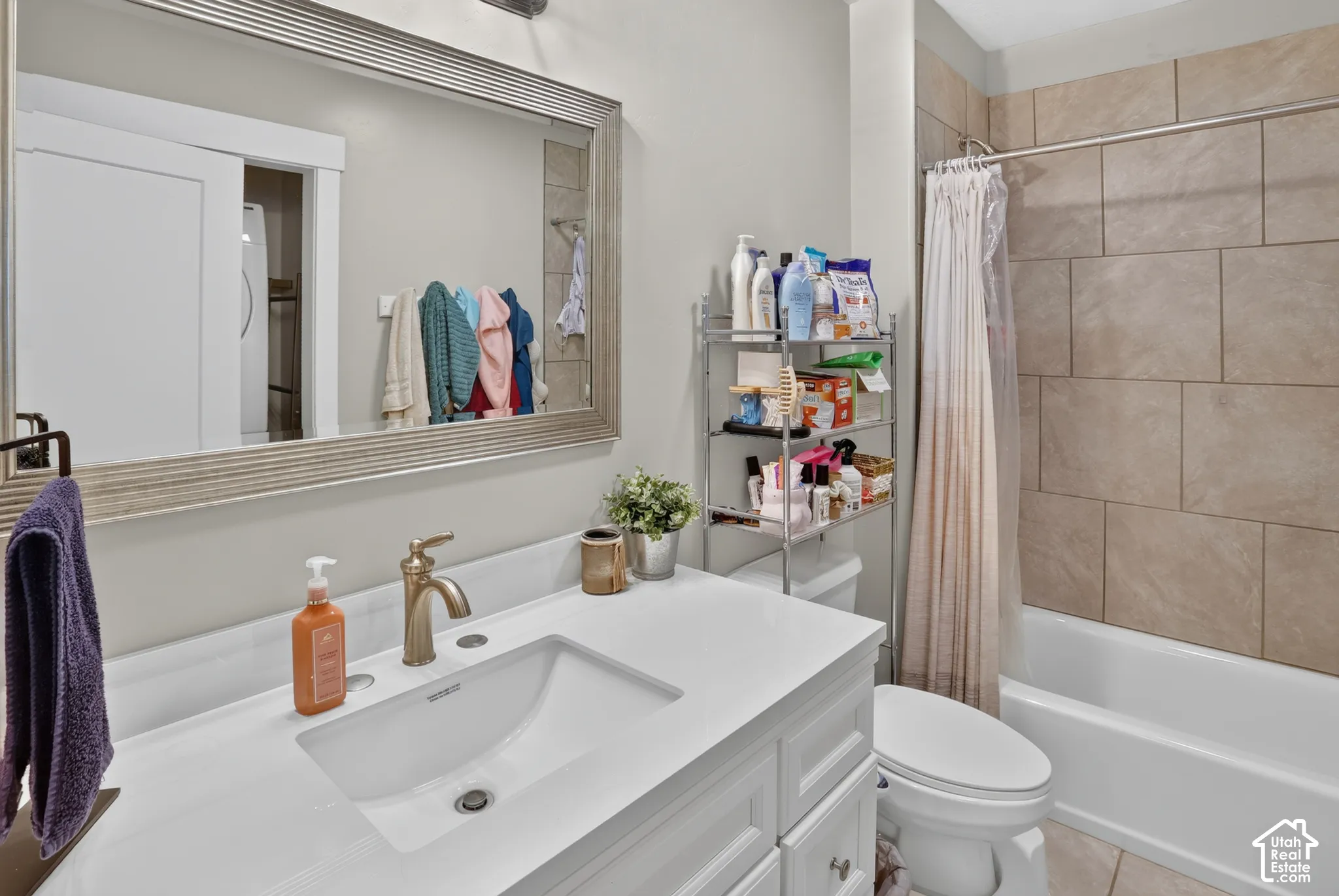 White vanity with an integrated sink and light-toned solid surface countertop, metallic faucet, large framed wall mirror, and neutral-toned rectangular tile shower surround