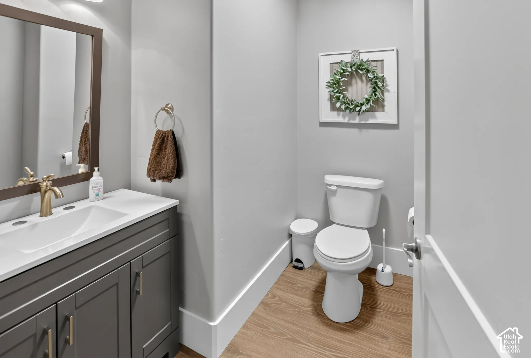 Dark gray shaker-style vanity with a solid surface countertop, integrated sink, and brass-finish faucet, complemented by wood-finish flooring
