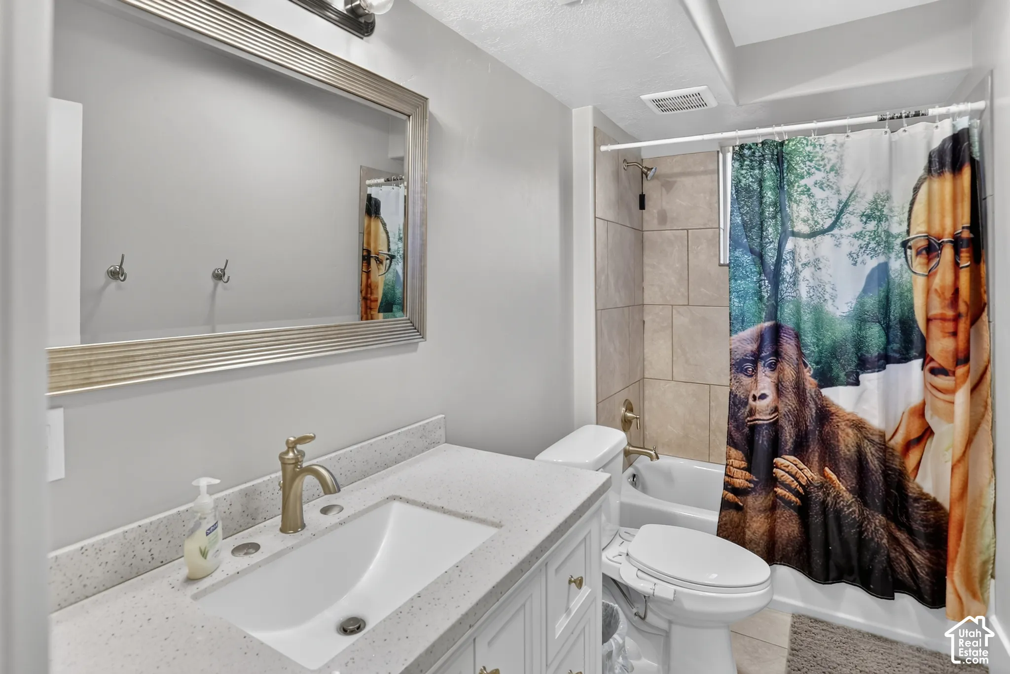 Bathroom vanity with a white undermount sink, speckled countertop, brushed-tone faucet, and a large framed mirror, featuring a tub-shower combination with neutral-toned wall tile