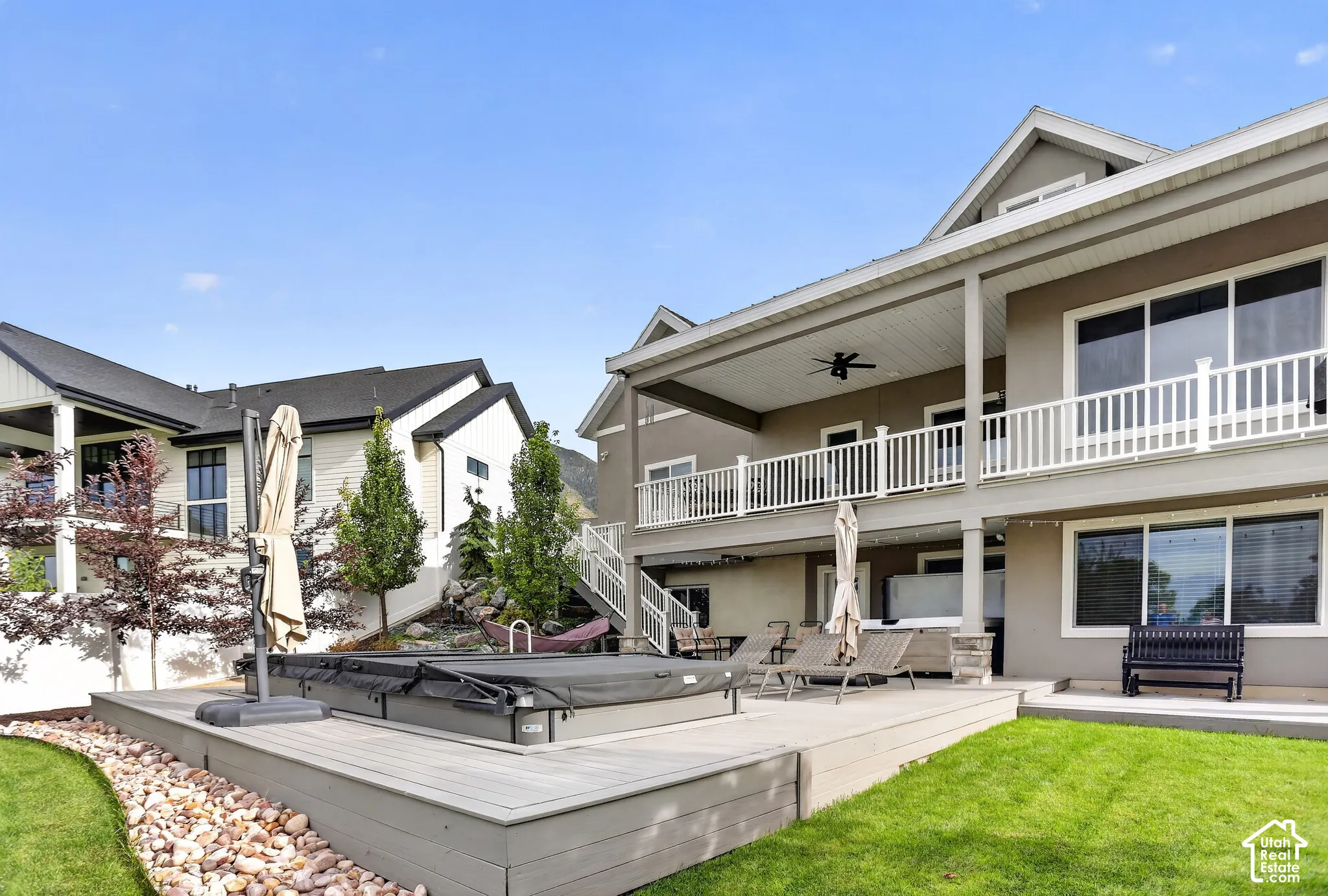 Multi-level exterior featuring a covered deck, second-story balcony with white railing, composite decking, and a built-in spa